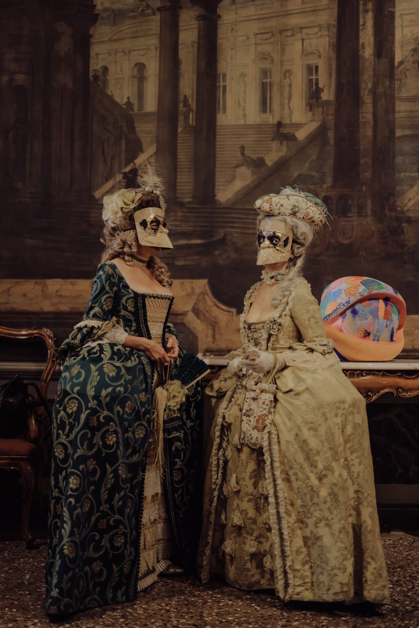 Women in traditional Venice Carnival costumes next to an eye-shaped sculpture