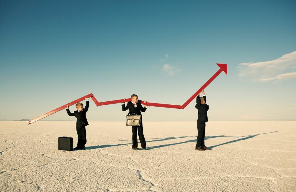 Three people wearing suits and holding a rising arrow in the middle of a desert.